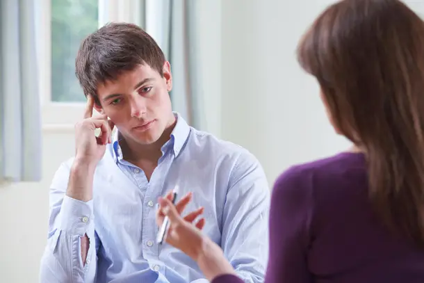 Young man listening thoughtfully to a therapist during a counselling session, symbolising a safe space for reflection and support.
