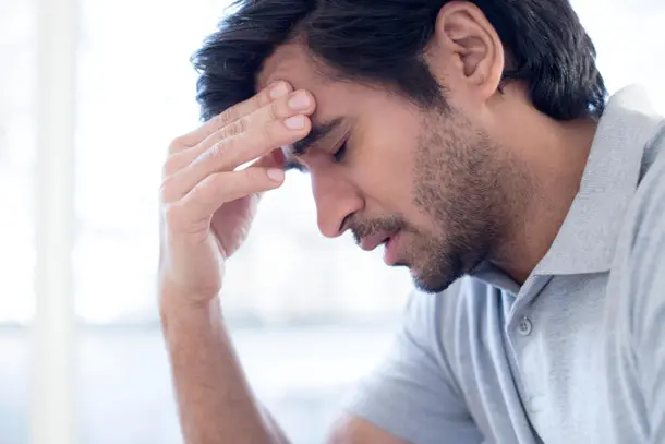 Man sitting with his hand on his forehead and eyes closed, appearing overwhelmed representing the impact of stress and the importance of seeking support