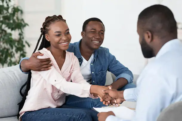 Smiling couple sitting together on a sofa, shaking hands with a therapist, symbolising trust and a positive step forward in counselling