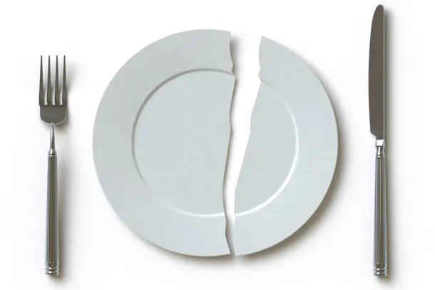 White plate broken into two pieces, placed between a fork and knife, symbolising difficulties with eating and the emotional impact of eating disorders