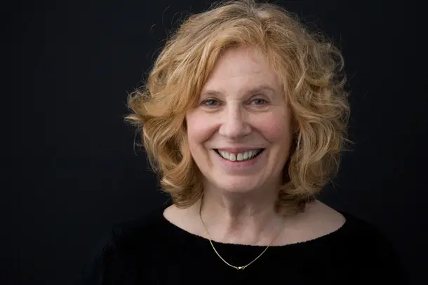 Portrait of a smiling woman with curly hair against a black background, conveying warmth and approachability.