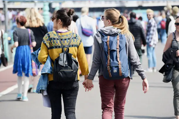Two women holding hands while walking outdoors in a busy public space, symbolising love, acceptance, and support for same-sex relationships