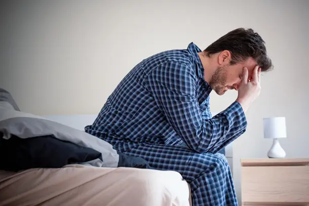 Man sitting on the edge of a bed in pyjamas with his head in his hand, appearing distressed symbolising sleeplessness, anxiety, or emotional struggle
