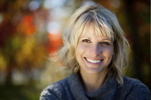 Smiling woman outdoors on a sunny day with colourful autumn leaves in the background, symbolising hope and positive change