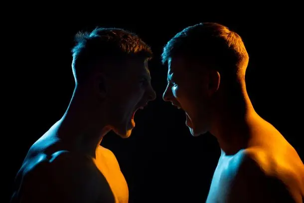 Two shirtless men facing each other and shouting in anger against a dark background, symbolising conflict and intense emotions that counselling can help address