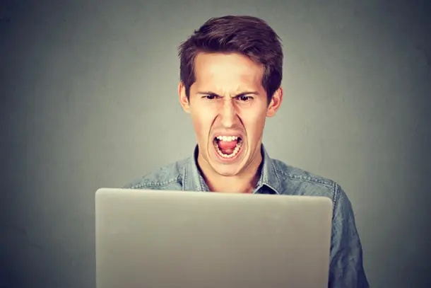 Young man sitting in front of a laptop, shouting in frustration, symbolising anger, stress, or emotional overwhelm.