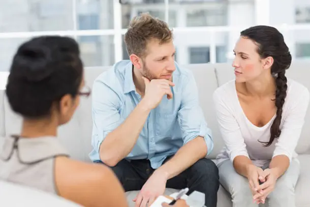 Couple sitting together on a sofa during a counselling session, having a thoughtful conversation with a therapist, symbolising open communication and support.
