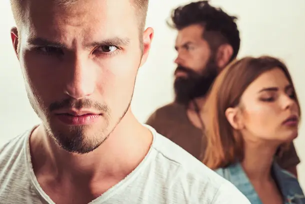 Close-up of a young man looking serious with two people blurred in the background, suggesting tension or conflict that could benefit from counselling support