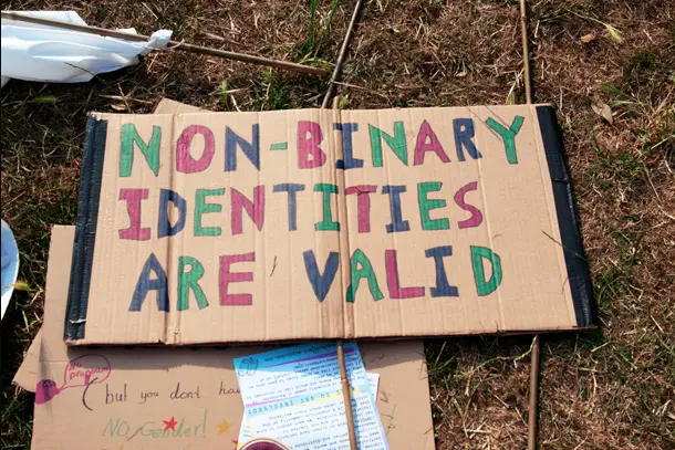 Handmade cardboard sign on the ground reading ‘Non-Binary Identities Are Valid,’ symbolising support and affirmation for gender-diverse individuals